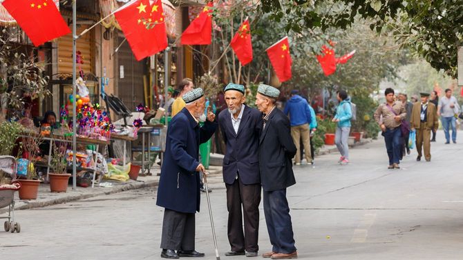 2017年10月、新疆ウイグル自治区・カシュガルにて。3人のウイグル人男性が会話をしている後ろには中国国旗がはためいている