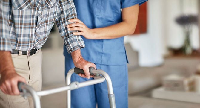 歩行器を使って歩く高齢男性と、サポートする介護士