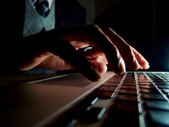 暗い室内でノートパソコンを使用する男性の手元