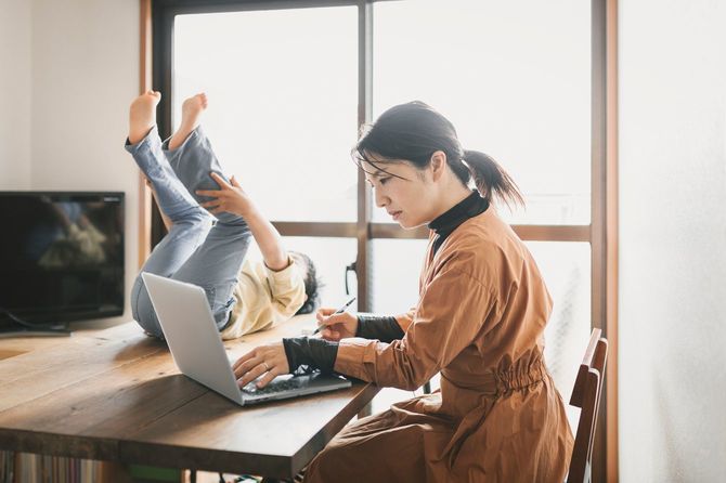在宅で働く母親のテーブルの上で遊んでいる息子