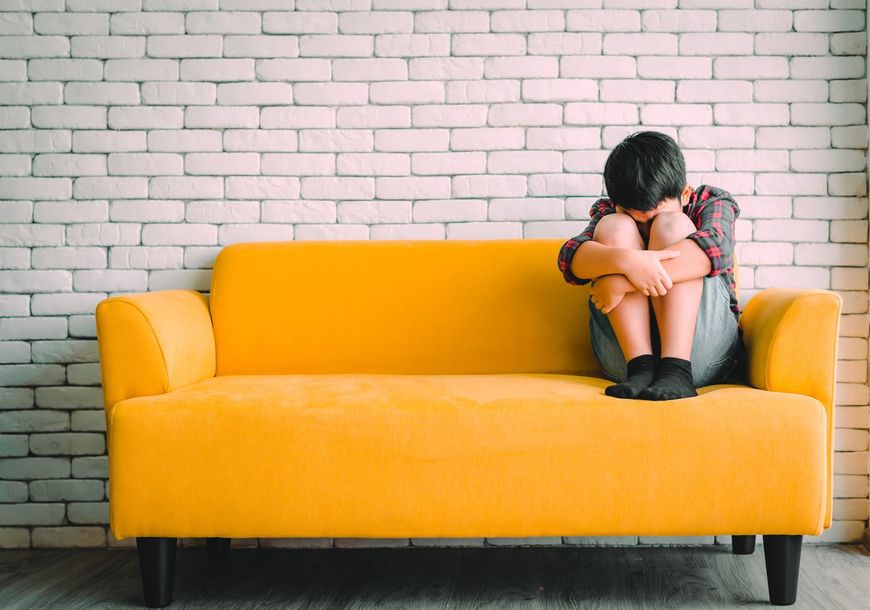 黄色のソファに座って悲しむ子供