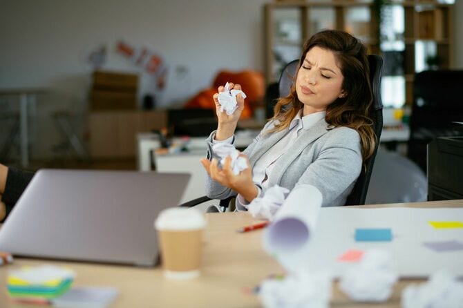 丸めた紙を両手に持ってデスクに座るビジネスウーマン