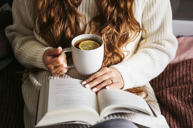ベッドで熱いお茶を飲みながら座り、本を読んでいる女性
