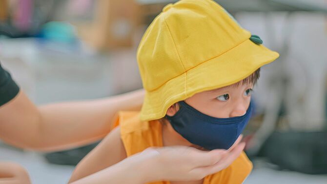 幼稚園児の息子にマスクと帽子をかぶせる母親の手元