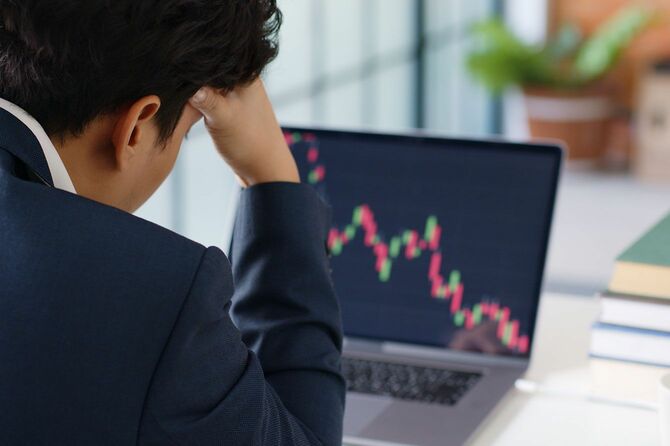 パソコンで株価チャートを見ながら頭を抱える男性
