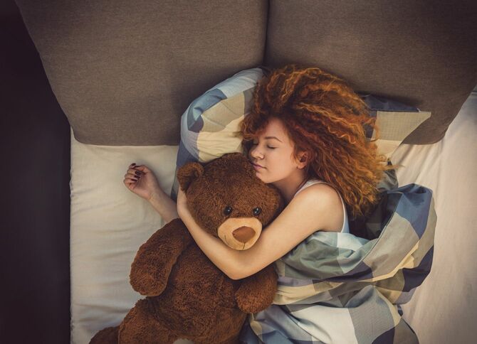 大きなクマのぬいぐるみを抱いて眠る女性