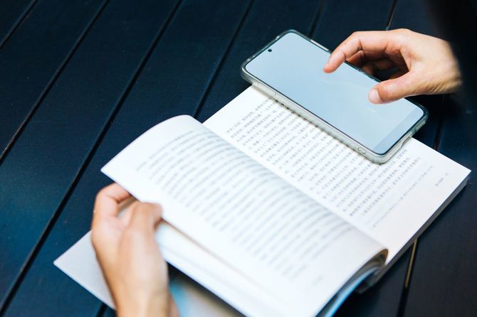 右手でスマホを使いながら、書籍を読んでいる人