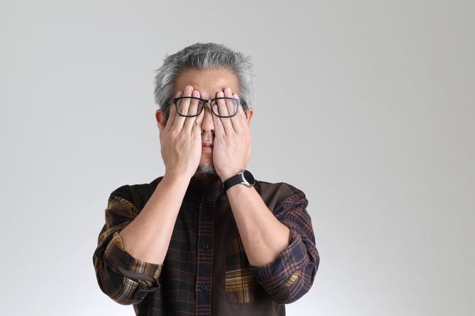 手で顔を覆う眼鏡のシニア男性