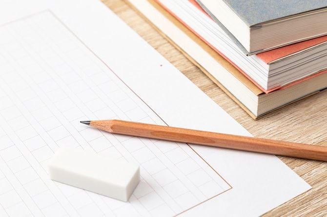 原稿用紙の上の鉛筆と消しゴム、横に積み上げられた本