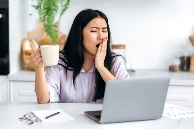 コーヒーを手にあくびをするビジネスウーマン