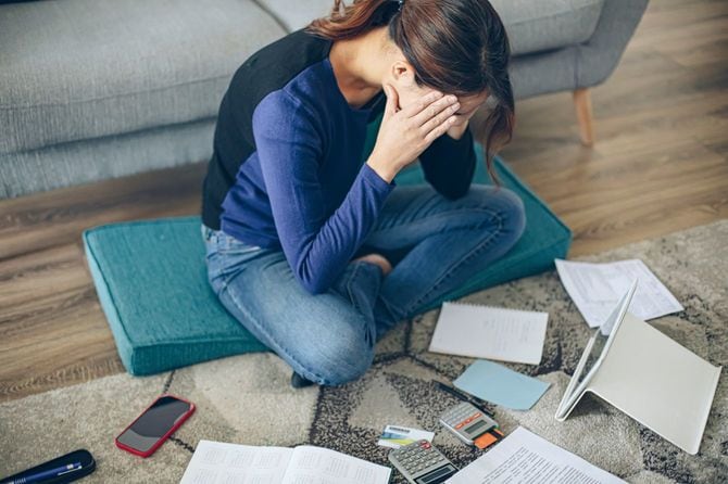 請求書を見ながらリビングルームの床に座って深刻な若い女性