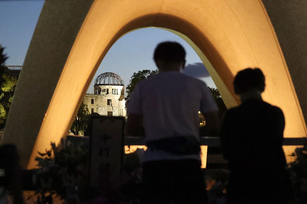 78回目の原爆忌を迎えた朝、平和記念公園の原爆死没者慰霊碑を訪れ、祈りをささげる人たち。奥は原爆ドーム＝2023年8月6日午前、広島市中区