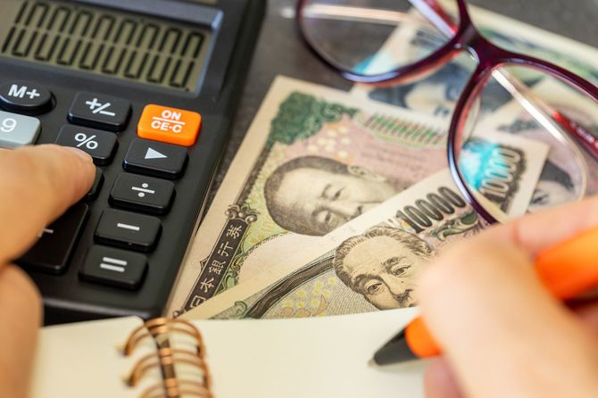 現金の上においた電卓で計算し、右手でメモを取っている