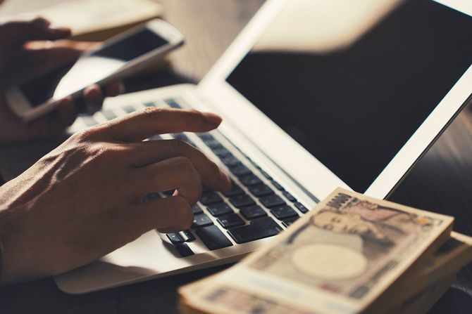 日本の札束とノートパソコンを扱う男性