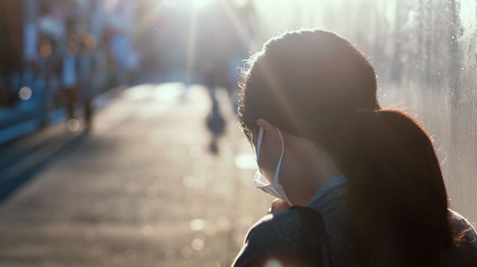 日差しの中、マスクを着用して歩く女性