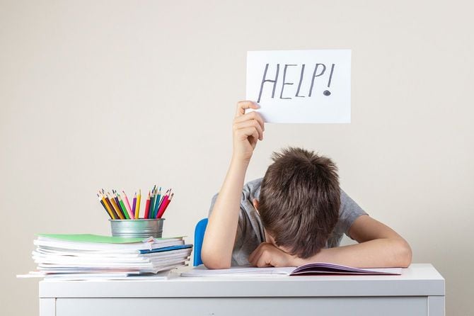 机に顔を伏せて「HELP！」と書いた紙を持つ子供