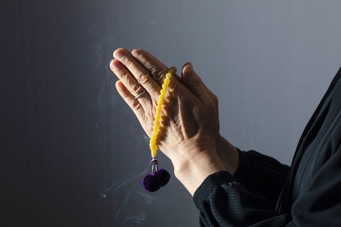 喪服を着て数珠を持って手を合わせる女性