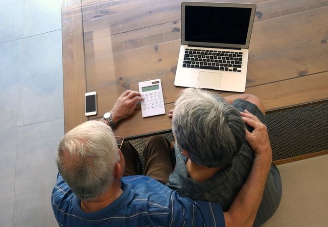 モダンなインテリア、Appleガジェットが机に並べられた空間で、裕福なシニアカップルが電卓を使用している