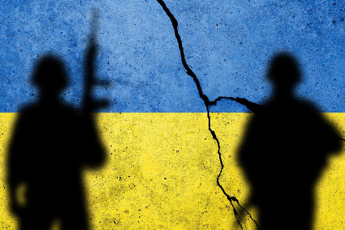 兵士のシルエットがあるコンクリートの壁に描かれたウクライナの国旗