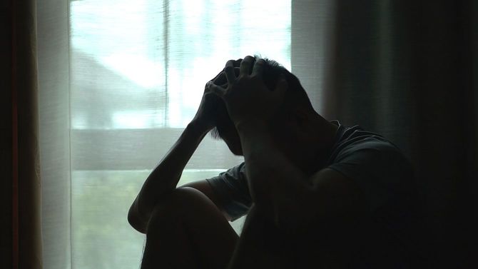 薄暗い部屋で頭を抱えて座っている男性