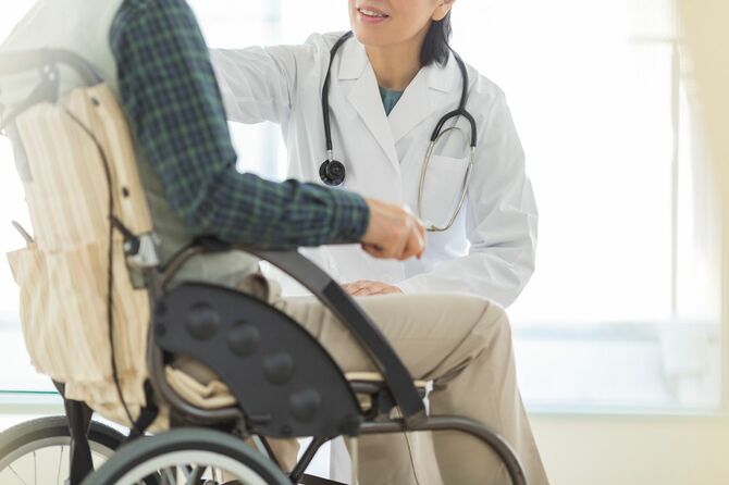車椅子にのったシニア男性に話しかける医師