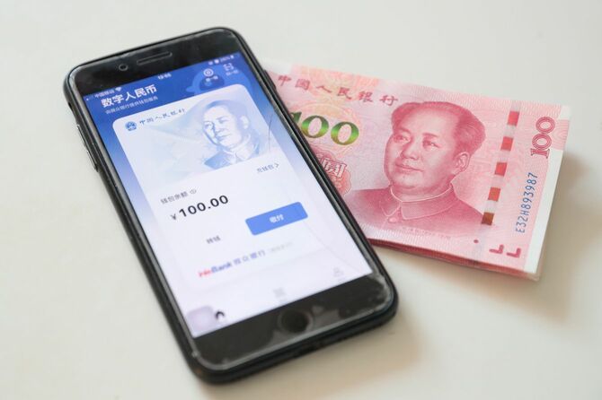 スマートフォンに表示されたデジタル人民元ウォレット（財布）アプリと人民元紙幣（2022年1月6日、中国・北京）