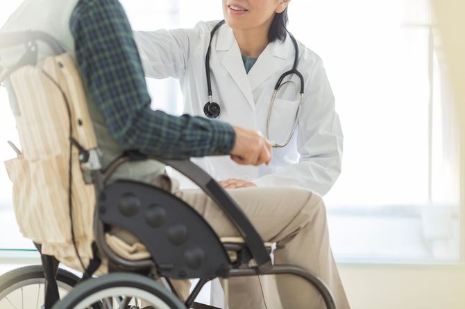 車椅子にのったシニア男性に話しかける医師