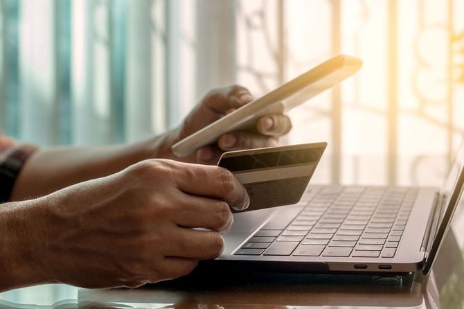 パソコンを前に、支払いのために携帯電話やクレジットカードを持つ人