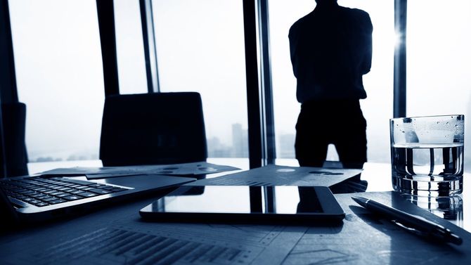 窓際に立って外を眺めるビジネスマン