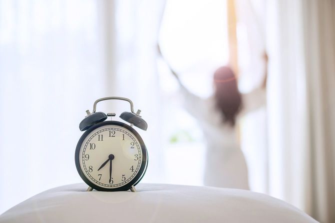 目覚まし時計と、カーテンを開ける女性