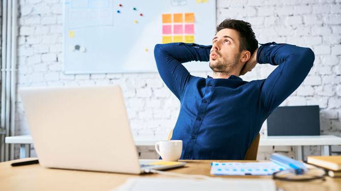 仕事の合間に手を頭の後ろで組んで椅子にもたれかかってリラックスする男性