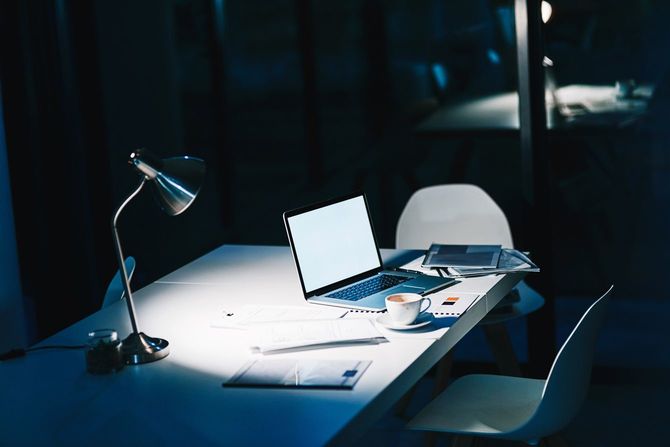 夜の遅い時間に残業していた痕跡。ノートパソコンとランプだけがともっているオフィスに今は人がいない