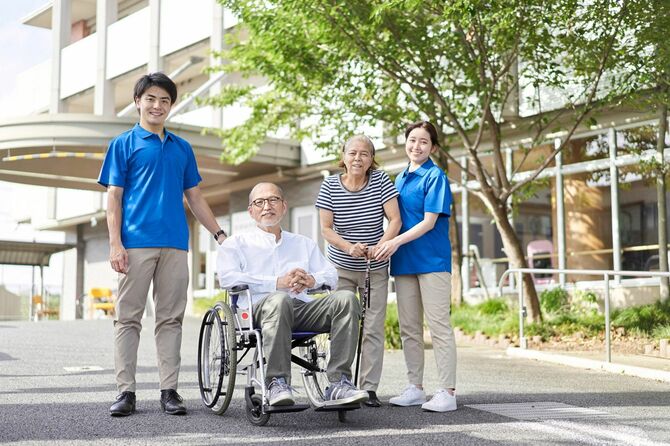 車椅子に乗る高齢者と伴侶、介護士