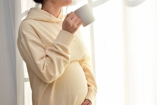 20代の妊婦がマグカップで飲み物を飲んでいる。