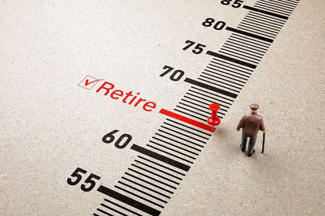 年齢の目盛りが書かれた紙の65歳の部分に「Retire」の文字と赤いピン、高齢男性のミニチュア人形が置かれている