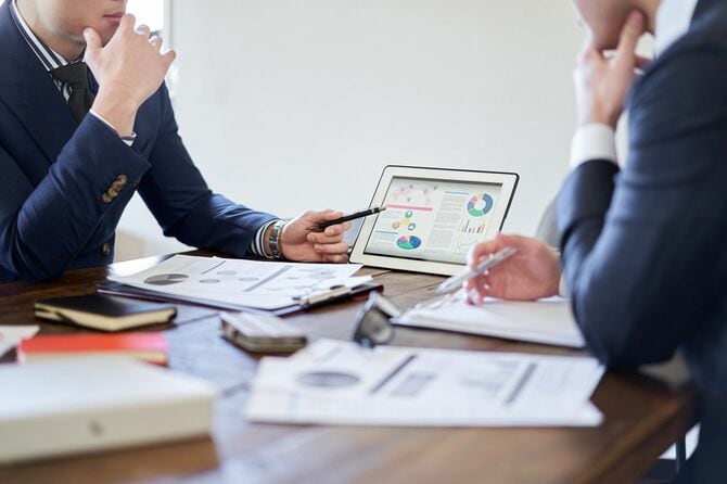 会議室で、タブレット端末の表を参照しながら話し合っているビジネスパーソン