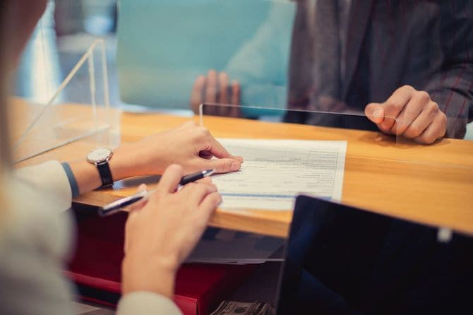 銀行の窓口係が契約書の部分を指さしながら、顧客に契約書を手渡そうとしている