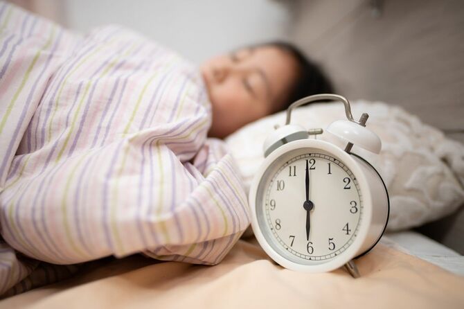 眠っている子供とベッドサイドの目覚まし時計