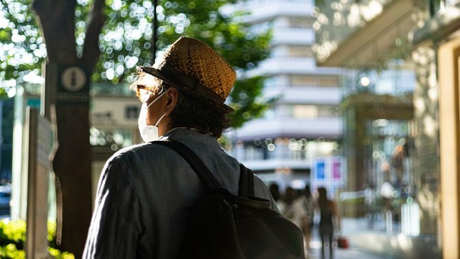 マスクをした男性が陽を浴びながら東京の街を歩く