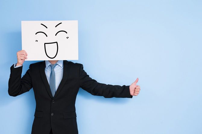 笑顔のイラストが描かれたボードを顔の前に持つ人