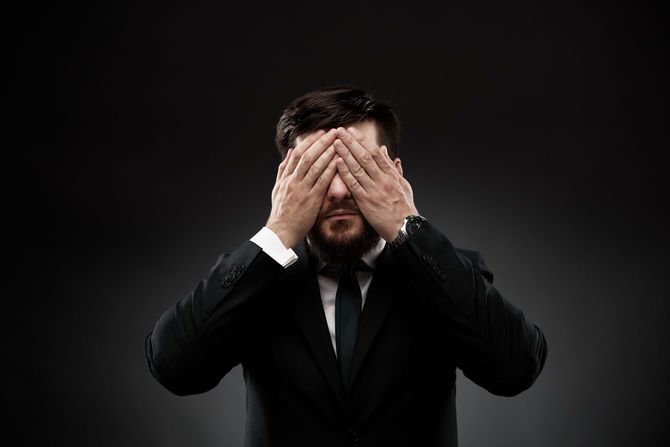手で目を覆って嘆くスーツを着た男性