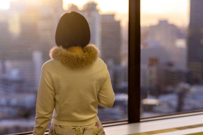 オフィスの窓から高層ビル群を眺める女性の後ろ姿