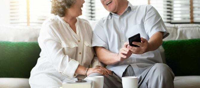 自宅で携帯電話を使用しながら笑うシニアカップル