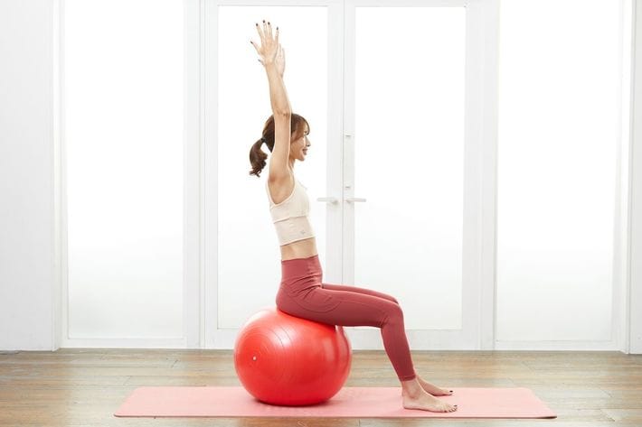 ［巻き肩の修正②］前方に上げた両腕を、そのまま耳の後ろに位置するまで上げます