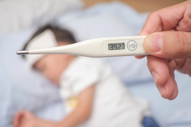 39.2度を表示する体温計と寝込んでいる子供
