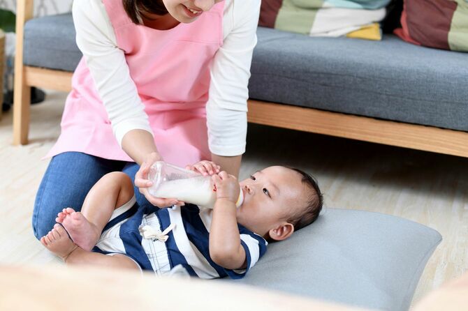 哺乳瓶でアジアの赤ん坊にミルクを与える女性保育士