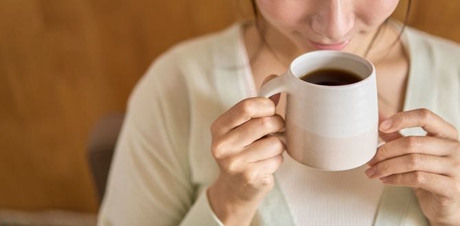 若い女性がソファーでくつろぎながらホットコーヒーを飲む