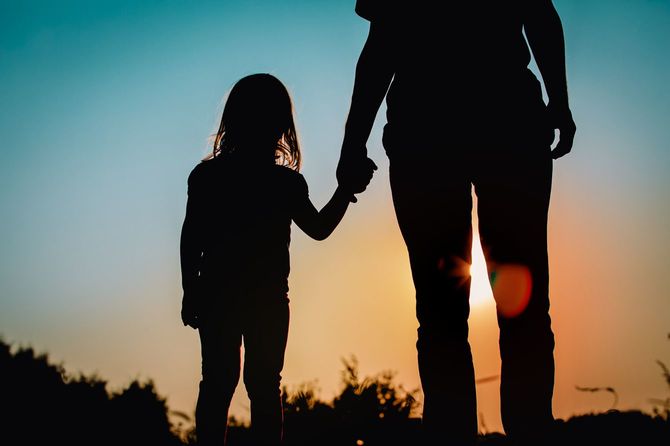 手をつないで夕焼けを見る親と娘