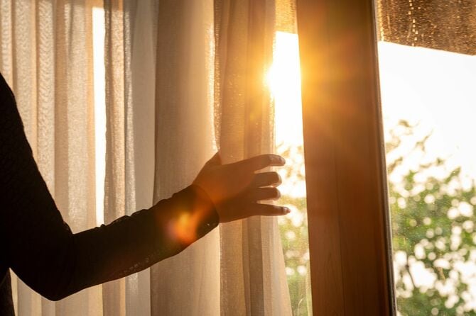 寝室の窓のカーテンを開く女性の手