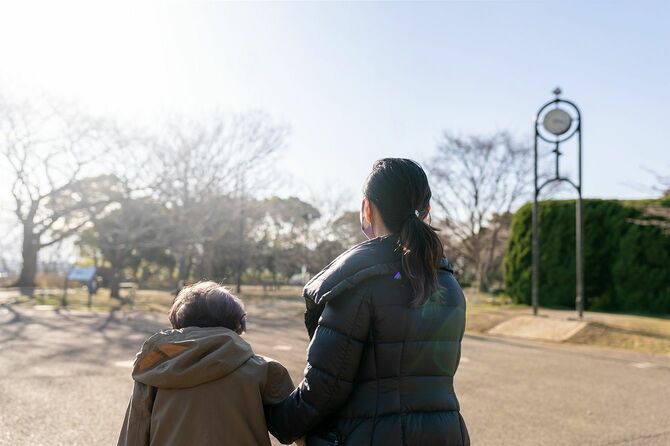 日本の介護スタッフは、日本の先輩女性が公園を散歩するのをサポートしています。